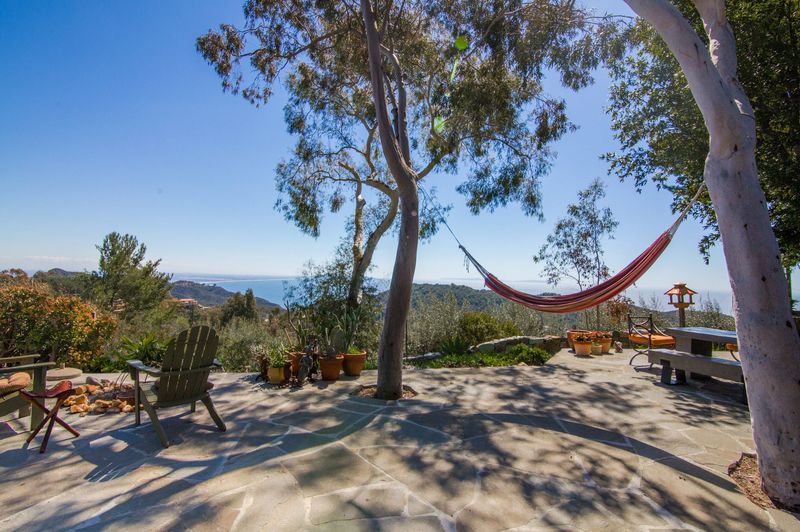 Outdoor stone patio with mountain and ocean views. A hammock hangs between two trees.